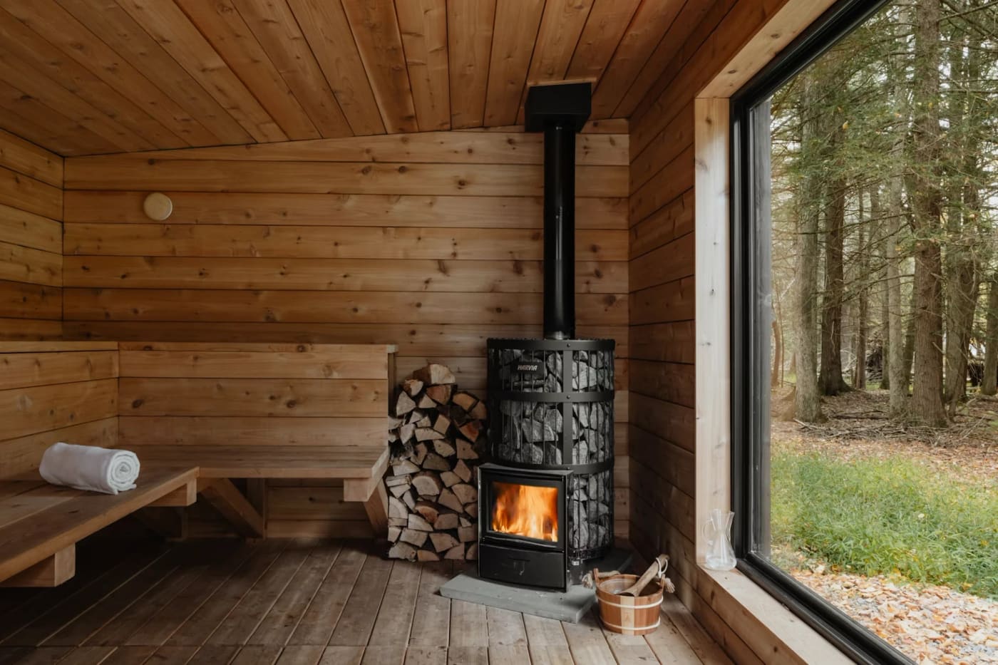 Badstue i tre med vedfyrt ovn og stort vindu ut mot skogen